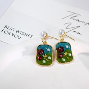 Macro detail of French vintage earrings with red rose, blue enamel and pearls