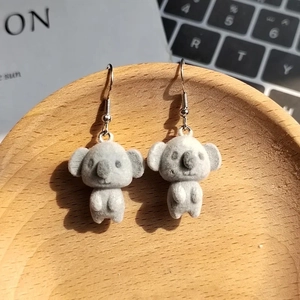 Cute gray flocked koala earrings with silver hooks displayed on a wooden stand