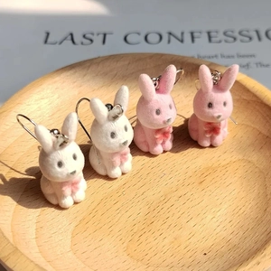 Close-up of cute flocked rabbit earrings in white and pink with tiny bow details