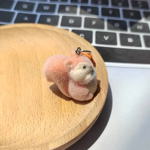 Cute pink and white flocked squirrel plush keychain with orange hook on a wooden tray