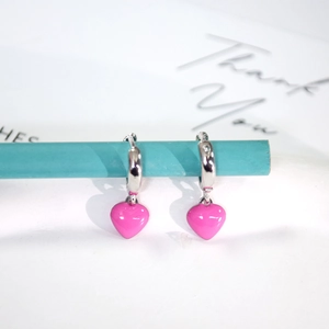 Detail of pink enamel heart earrings hanging on a silver hoop with polished metal finish