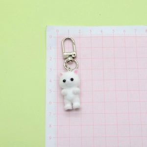 Cute white flocked kitten keychain with silver metal buckle on a scale background