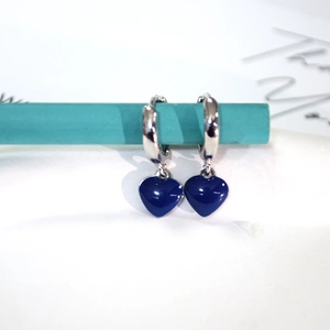 Macro detail of silver earrings with deep blue enamel heart charms on a stand