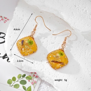 Detail of handmade resin earrings with yellow dried flowers and gold wire wrapping