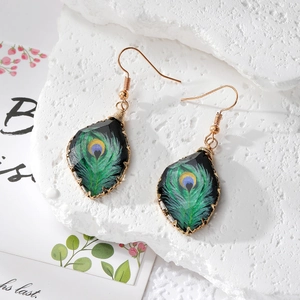 Detail of teardrop resin earrings featuring peacock feather patterns and gold wire wrapping