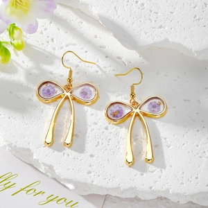 Close-up of golden bow earrings with purple dried flowers and gold foil accents