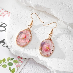 Handmade gold earrings with pink dried flowers and pearls in resin on white stone