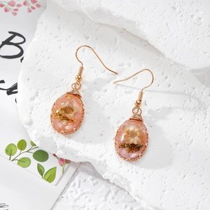 Macro detail of teardrop resin earring with pink dried flower and gold foil flakes