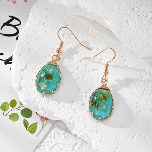Close-up of gold handmade wire-wrapped earrings with dried green flowers and gold foil