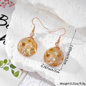 Détail de boucles d'oreilles en résine avec fleurs séchées jaunes et feuilles d'or