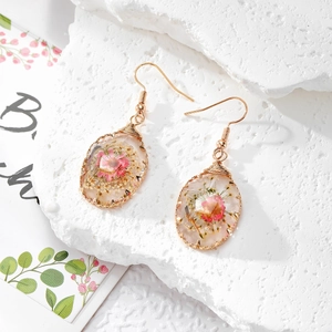 Detail of handmade resin drop earrings with pink dried flowers and gold wire wrap