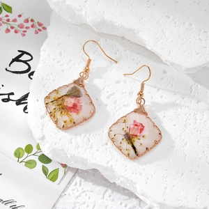 Détail de boucles d'oreilles carrées en résine avec fleurs séchées et fil doré