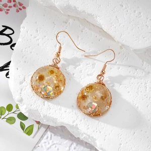 Gros plan de boucles d'oreilles dorées avec fleurs séchées jaunes en résine époxy