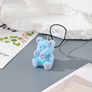 Macro shot of a light blue flocked bear keychain with pink bow and ribbon on stone props