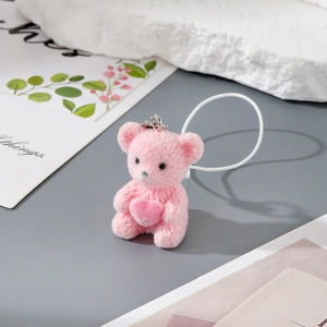 Detailed close-up of a pink flocked bear keychain with heart decor on a gray surface