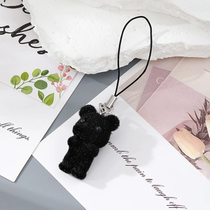 Close-up of black flocked bear keychain with silver metal clasp on a scenic background