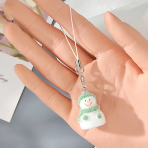 Close-up of adorable flocked snowman keychain with green hat and scarf on a cozy background