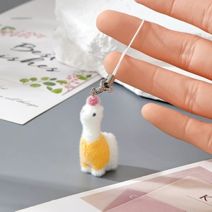 Close-up of white flocked alpaca charm with yellow knitted vest and red pompom detail