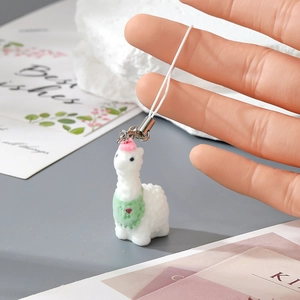 Close-up of white flocked alpaca keychain with pink hat and green scarf on hand