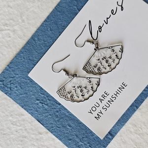 Close-up of translucent white fan-shaped acrylic earrings with black calligraphy details