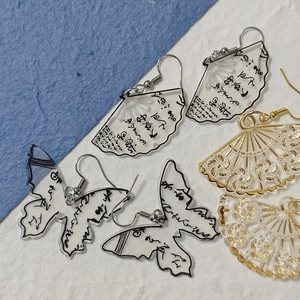 Macro detail of acrylic fan and butterfly earrings with Chinese calligraphy patterns