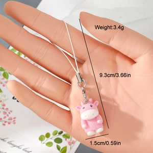 Pink flocked resin cow keychain charm with white woven strap held by hand