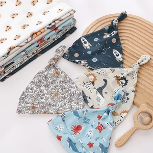 Detail of four patterned newborn knot hats featuring dinosaur and floral prints on cotton