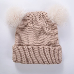 Détail du bonnet en tricot kaki avec deux grands pompons en fausse fourrure beige