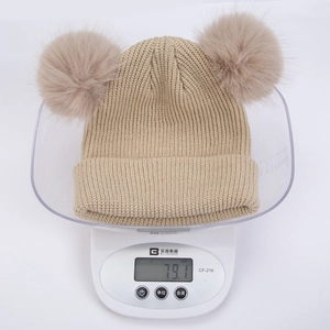 Détail montrant le poids de 79,1g pour le bonnet en tricot beige à deux pompons pour bébé