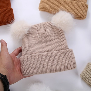 Détail du bonnet tricoté pour bébé avec deux pompons en fourrure synthétique beige