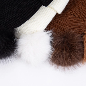 Détail de la maille et des grands pompons en fausse fourrure sur trois bonnets d'hiver