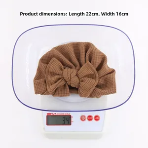 Détail du bonnet turban marron en maille gaufrée pour bébé sur balance pesant 34g