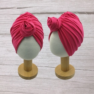 Front and side view of hot pink baby turban hat with a 3D rose knot on a wooden stand