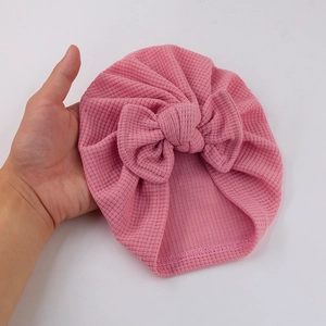 Détail du tissu gaufré rose et du grand nœud sur le bonnet turban pour bébé