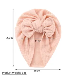 Bonnet turban rose en maille gaufrée pour bébé avec un grand nœud sur fond blanc