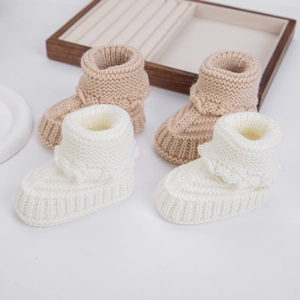 Detailed texture of cable knit baby booties in beige and white cotton blend material