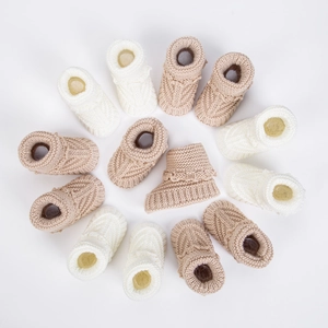 Close-up of cable knit baby booties in cream and camel with scalloped edge detail