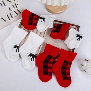 Detailansicht der Weihnachts-Babysocken mit Rentierprint und Karomuster auf Holz