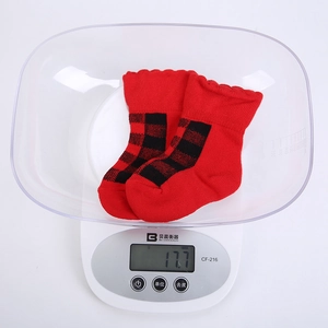 Detailansicht rot-schwarz karierter Babysocken auf Waage, zeigt Gewicht von 17,7g