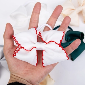 Detail of white grosgrain ribbon bow with red wavy edge embroidery on nylon hairband