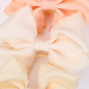 Detailed view of grosgrain ribbon bows with scalloped lace edges in soft pastel colors