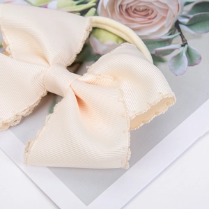 Macro detail of cream nylon baby headband with embroidered lace trim and ribbed texture bow