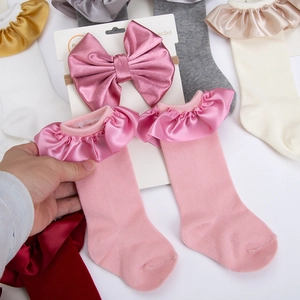 Close-up of pink baby socks with satin ruffles and matching bow headband set