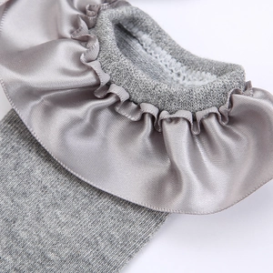 Detailed close-up of light gray knitted baby socks featuring silky satin ruffle trim details