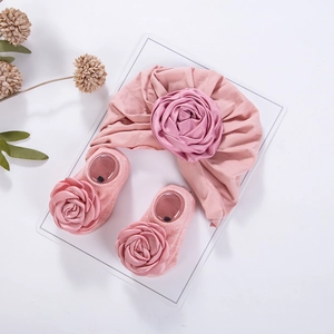 Detailansicht von Baby-Turban-Stirnband und Socken-Set mit rosa Satinrosen auf Karton