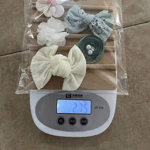 Detailed set of 5 chiffon flower and bow headbands for babies on a scale weighing 27.5g