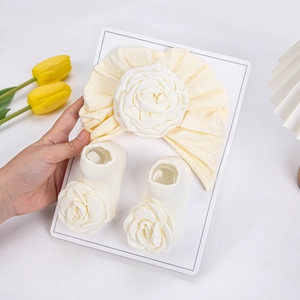 Detail von cremefarbenem Baby-Turban und Socken-Set mit großen Stoffrosen auf Karton