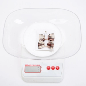 Macro view of two brown plaid fabric bow hair clips weighing five grams on a digital scale