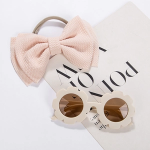 Flat lay of pink waffle bow headband and cream flower sunglasses for kids on magazine