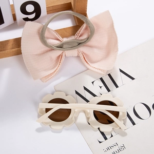 Close-up of pink bow headband and beige sunflower sunglasses for kids stylish summer set